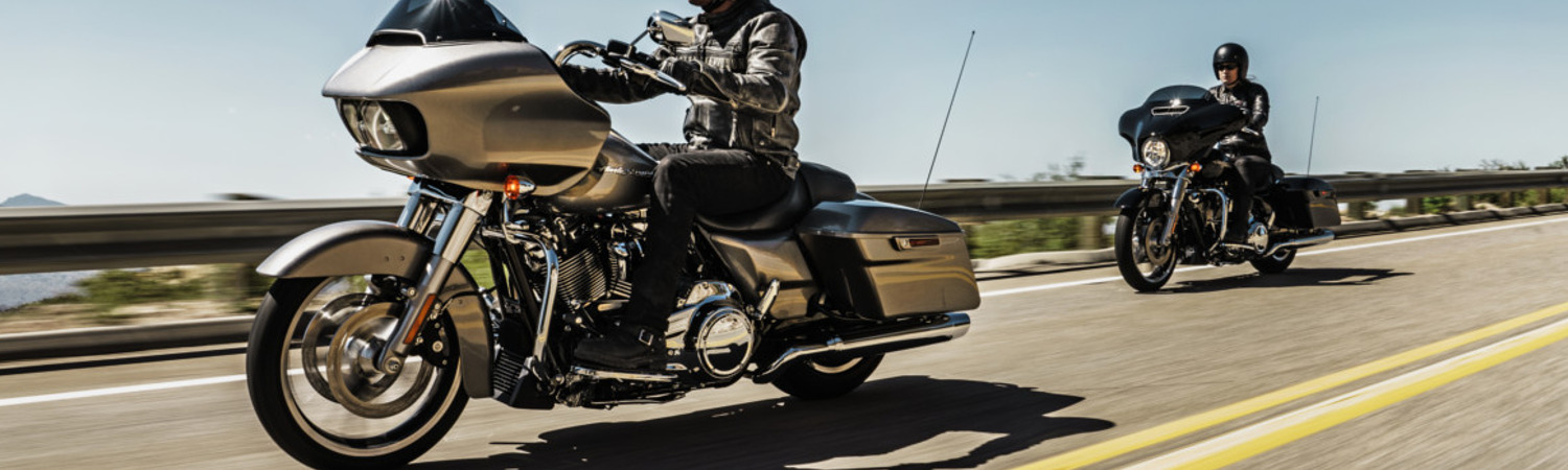 Two people riding Harley Davidson® Road Glide® motorcycles down a highway road next to a cliff